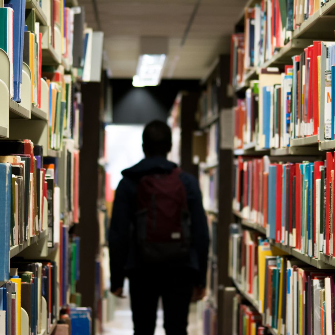 Solidaire pour les étudiants-homme de dos avec un sac à dos dans un un lieu contenant des rayonnages de documents archivés